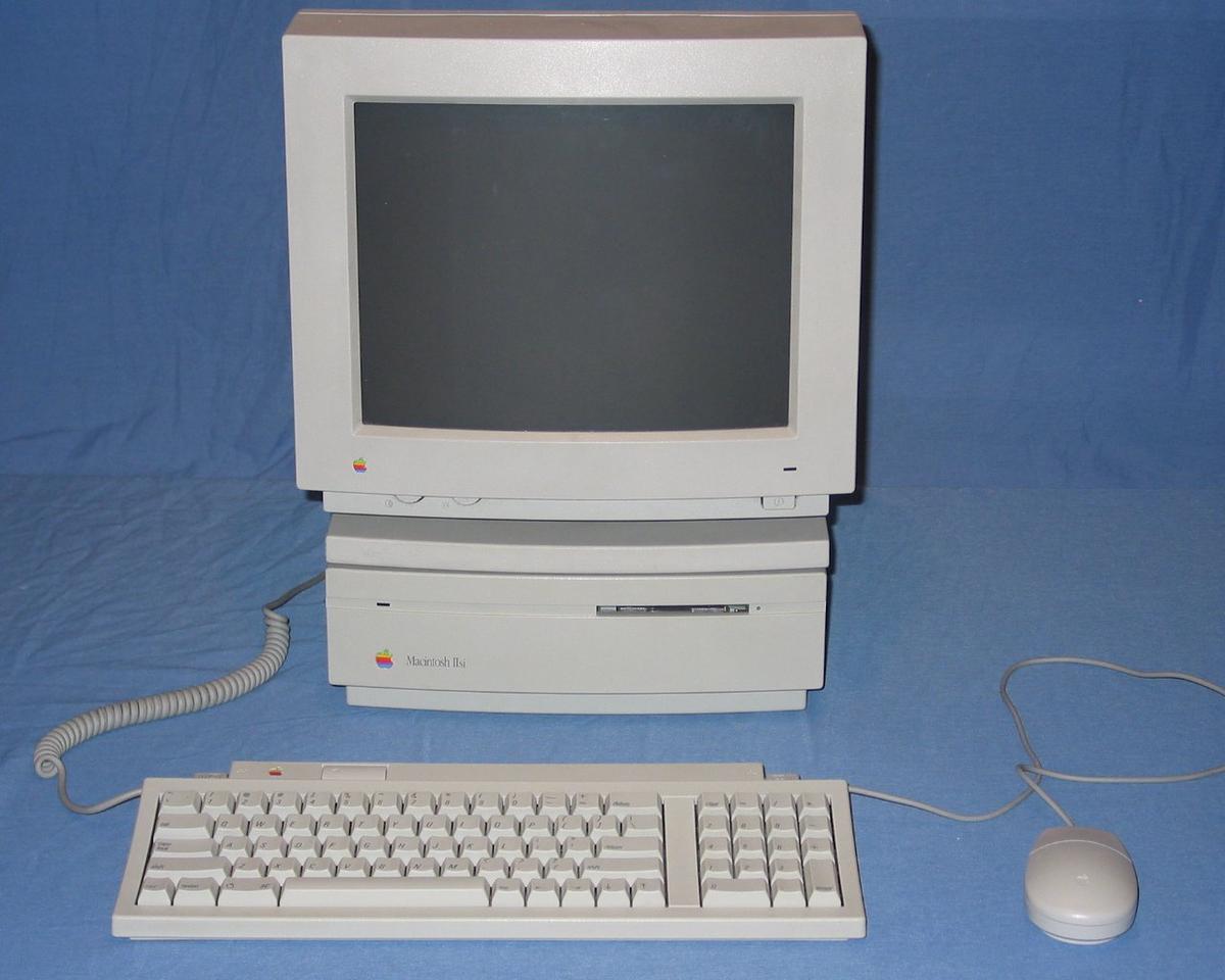 Der originale Macintosh Computer mit seiner ikonischen Maus und Tastatur auf einem Schreibtisch.